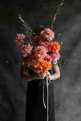 A person holding a bouquet of pink and orange roses with green foliage against a dark background.