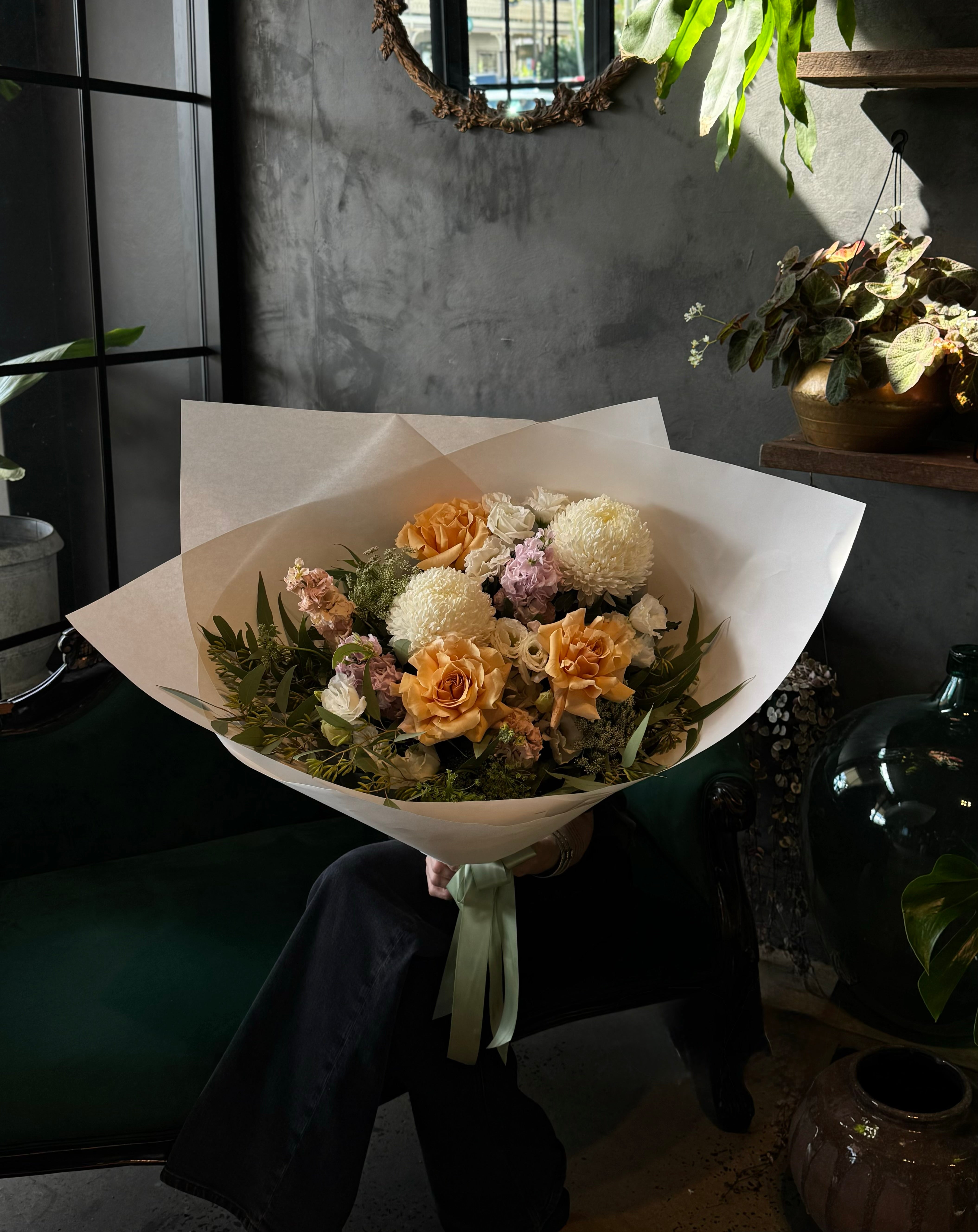 A bouquet of flowers including roses and other seasonal blooms, wrapped in card with a ribbon, on a dark background.