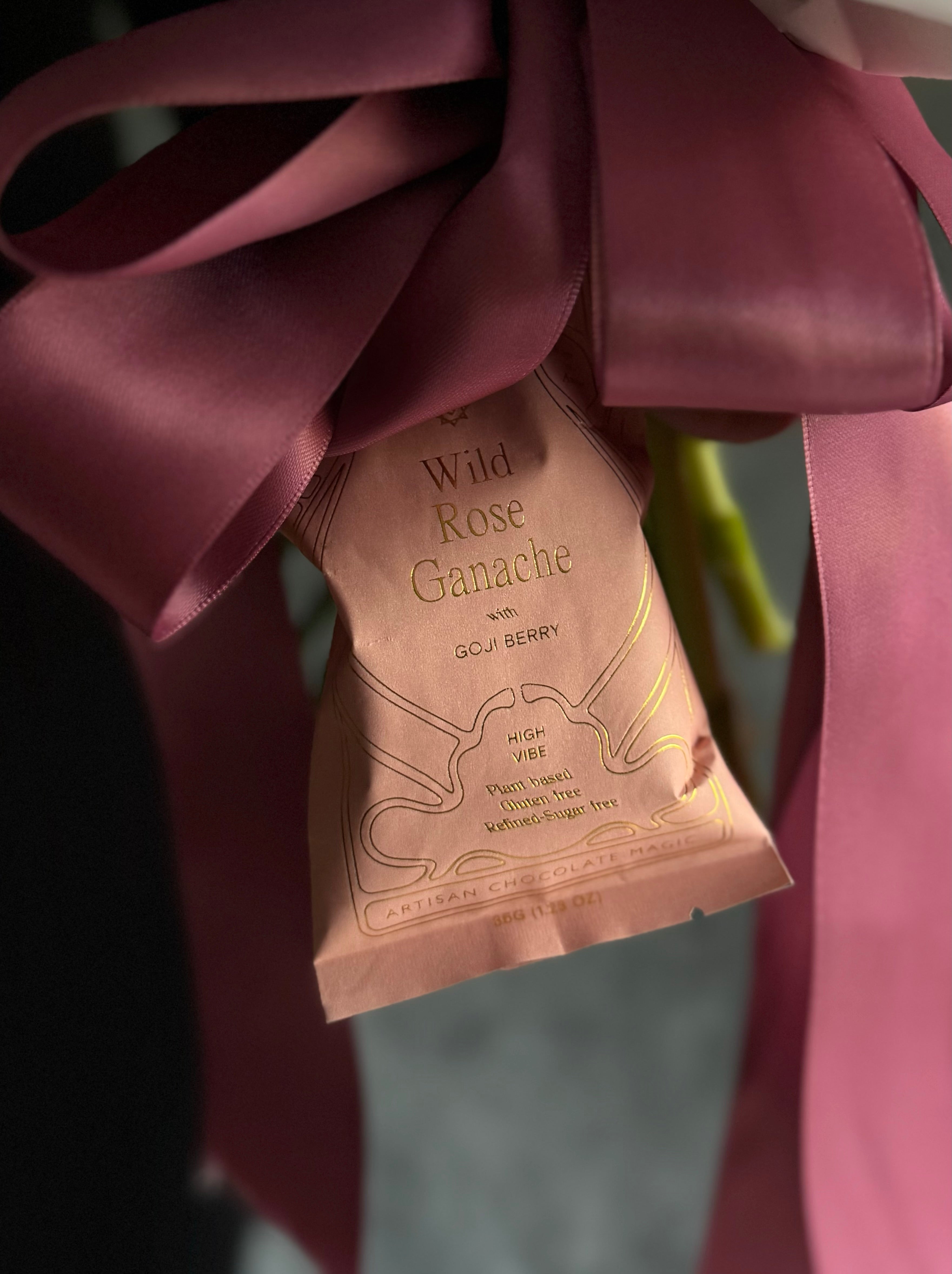 Close-up of a pink package labeled “Wild Rose Ganache with Goji Berry,” tied with a large mauve ribbon.
